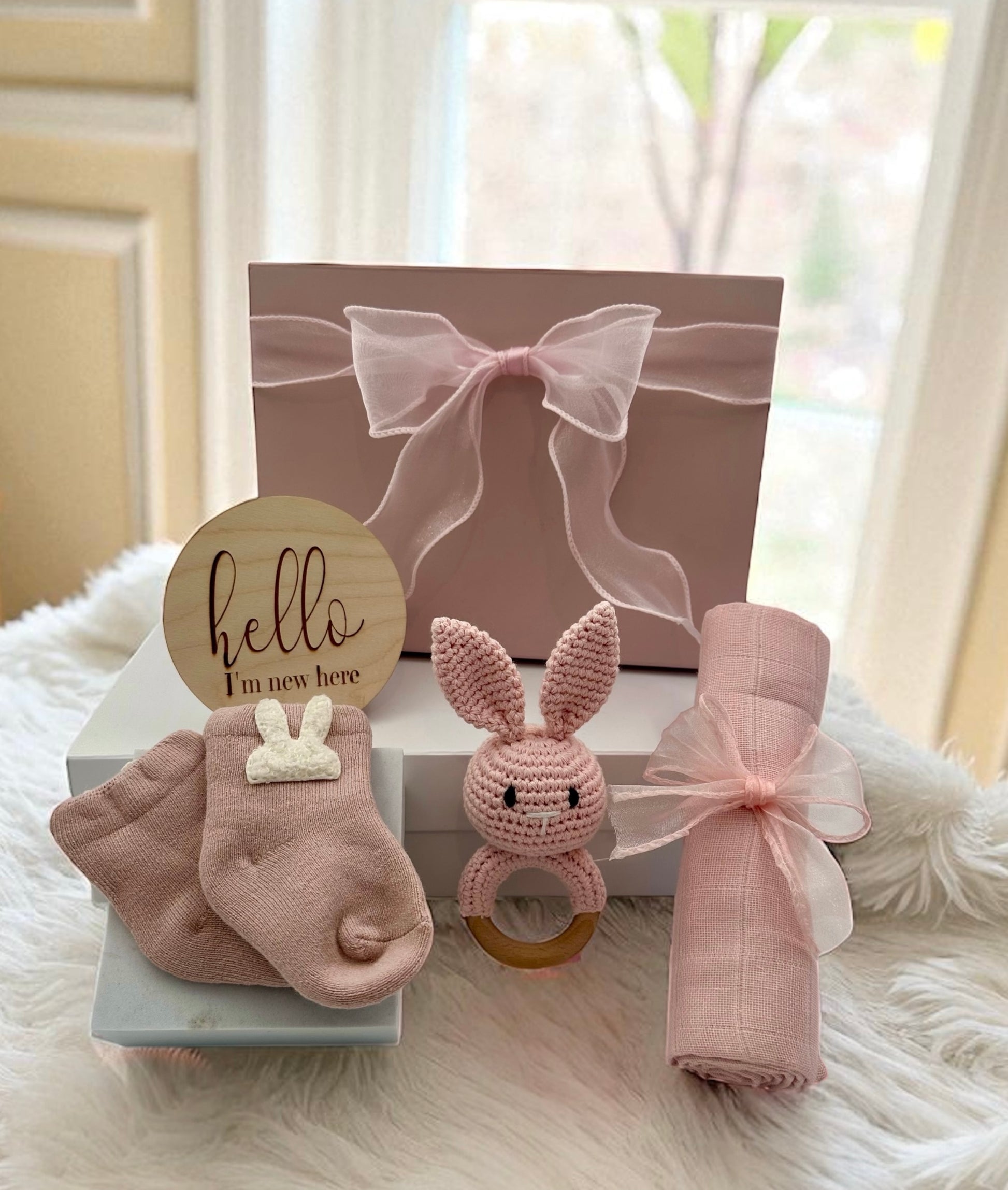 Baby Girl Gift Set featuring soft pink bunny socks, pink bunny rattle, gentle muslin cloth, and “Hello, I’m New Here” plaque for a newborn.