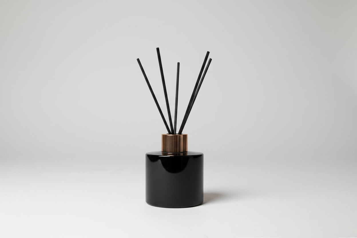 Black diffuser with sticks on a white surface, with a blurred background of stationery items.