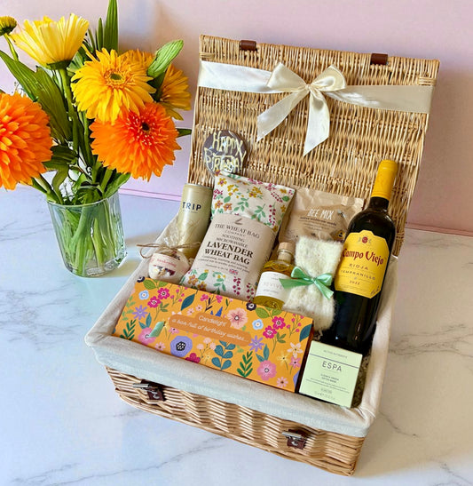 Gift basket with flowers, wine, and other items on a marble surface