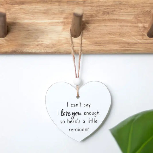 Heart shaped sentiment sign with "I Can't Say I Love You Enough" message hanging on wooden peg.