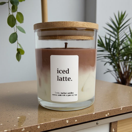 Candle labeled 'iced latte' on a wooden surface with plants in the background