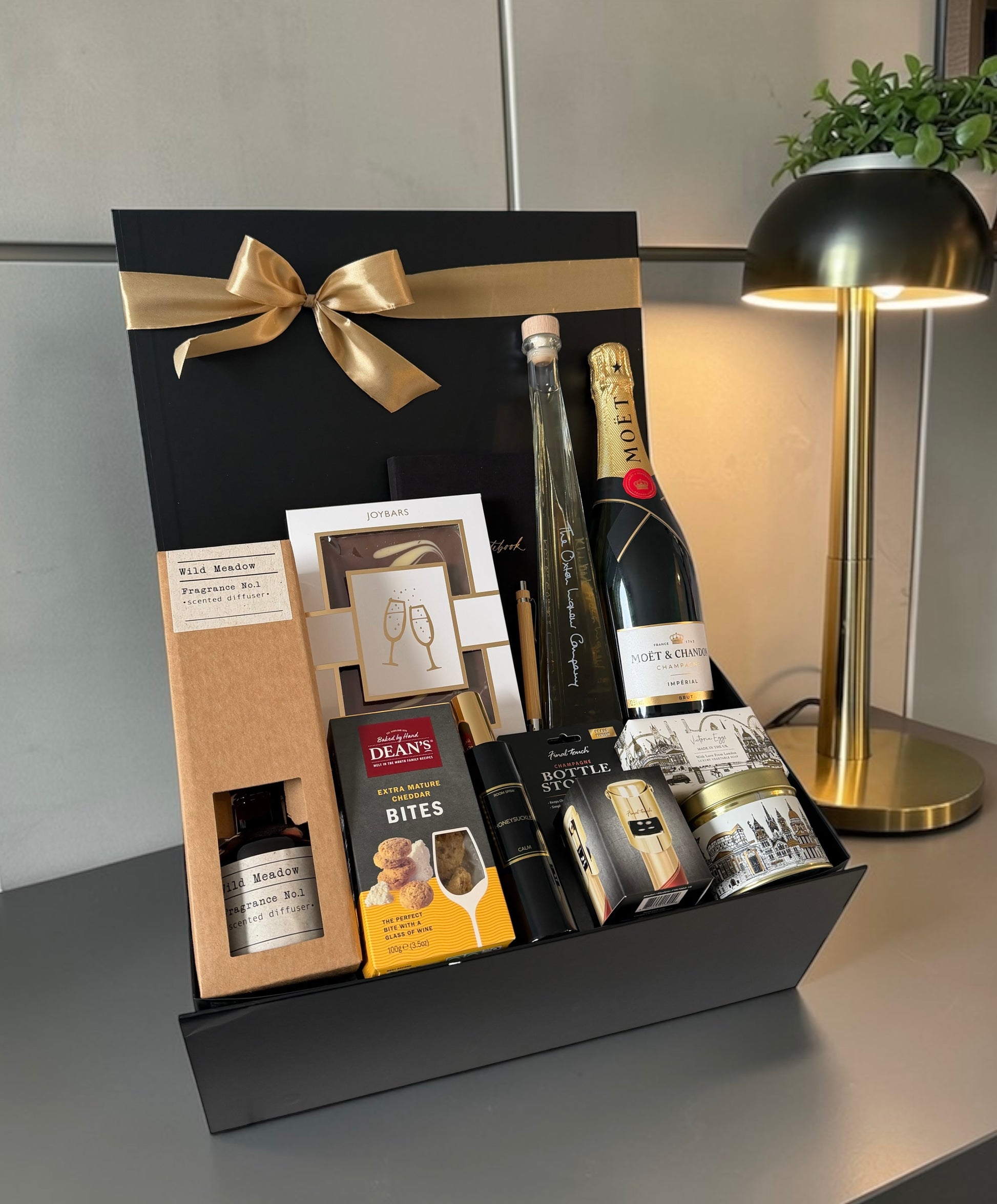 Premium congratulations gift hamper with chocolate, notebook, reed diffuser, gourmet cheese bites, rhubarb vodka liqueur and champagne.