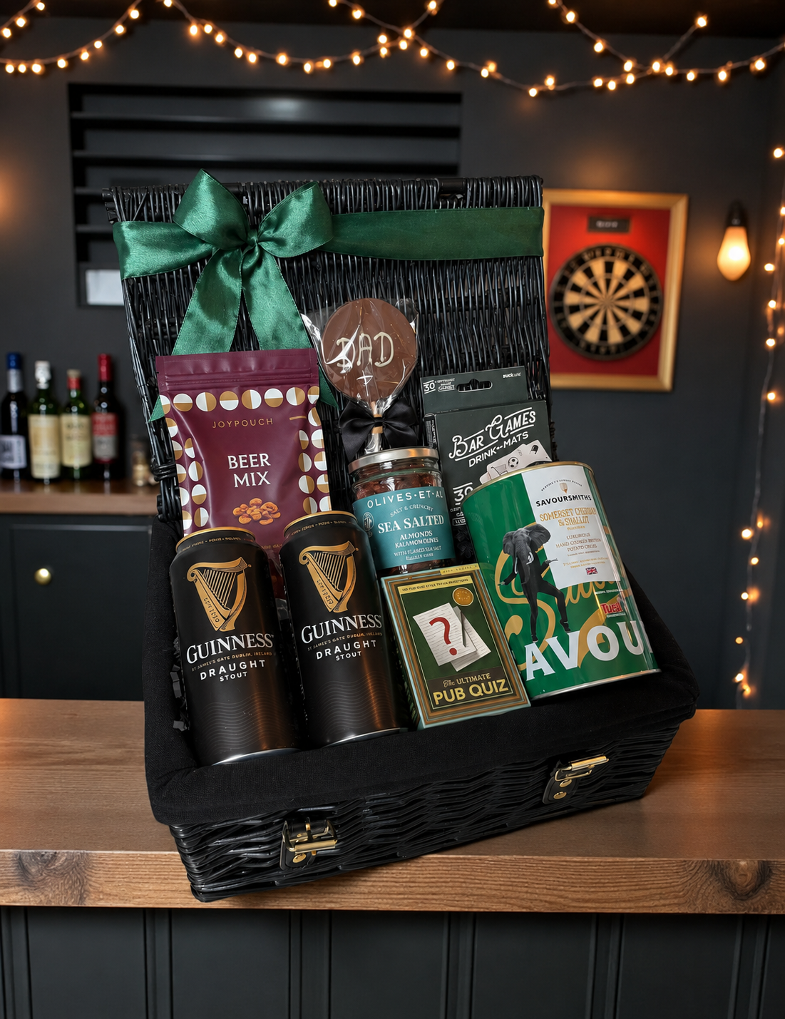 Gift basket with Guinness beer, snacks, and games on a wooden table with a dark background.