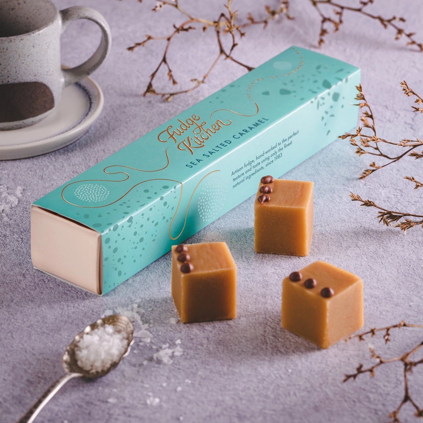 Box of Fudge Kitchen sea salted caramel fudge with a cup of coffee and decorative elements on a light background