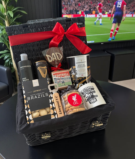 Gift basket with snacks and drinks on a table in front of a television showing a football match.