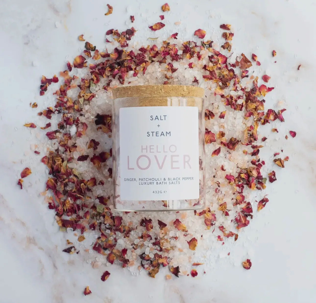 Hello Lover Salt and Steam bath salts in a jar surrounded by rose petals on a marble surface.