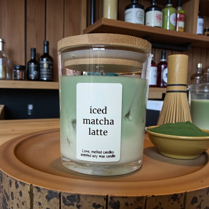 Candle labeled 'iced matcha latte' on a wooden surface with a bowl of matcha powder.