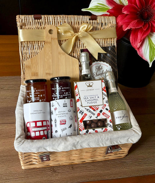 Gift basket with a cutting board, snacks, and a bottle of wine on a wooden surface.