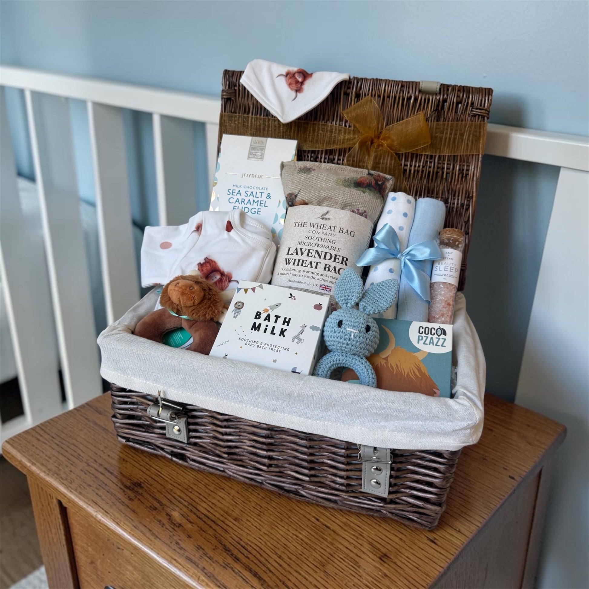 Highland Cow baby gift hamper with sleepsuit, bib, rattles, muslin cloths, wheat bag and treats for parents.