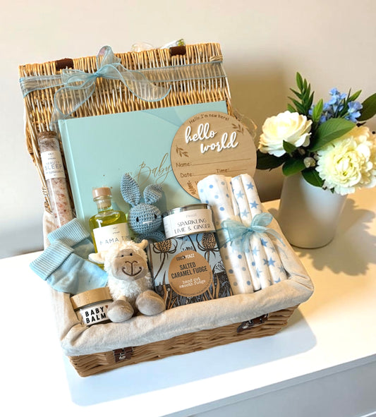 Baby gift basket with toys and items on a white surface with flowers in the background