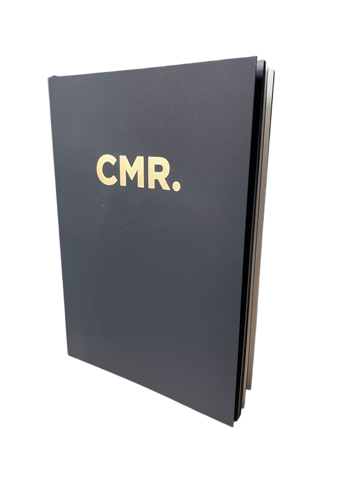 Branded notebook with black cover featuring gold "CMR." logo.
