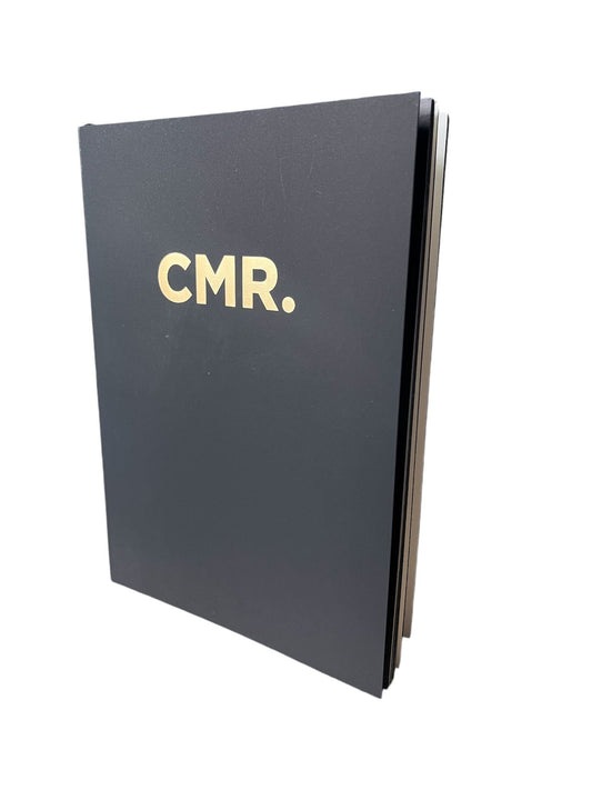 Branded notebook with black cover featuring gold "CMR." logo.