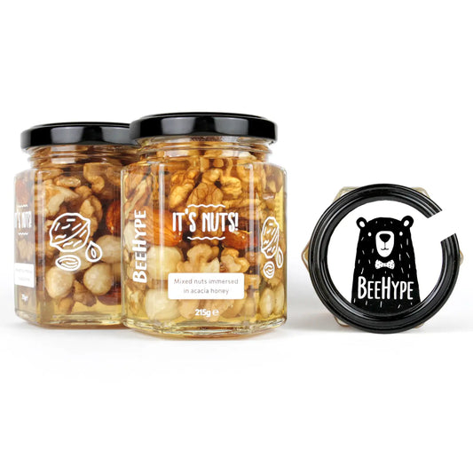 Mixed nuts in acacia honey jars with black lids, featuring walnuts, almonds, hazelnuts, and cashews.