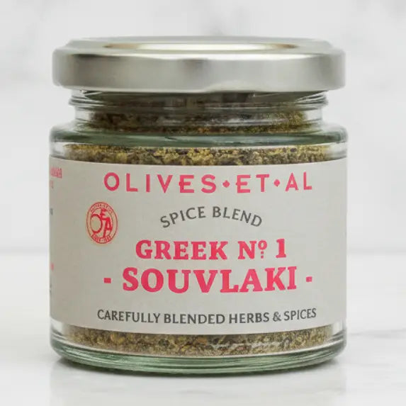 A glass jar of Olives Et Al Greek No. 1 Souvlaki spice blend with a silver metal lid and a white label featuring pink and black text, set against a clean white background.