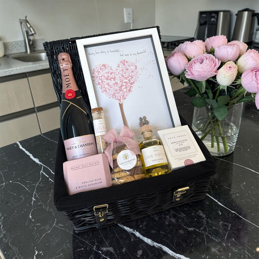 Romantic gift hamper with Moët & Chandon Rosé, rose candle, bath products, chocolates and love-themed framed artwork.