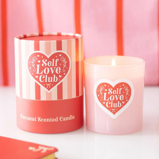 Pink candle with 'Self Love Club' heart design next to its striped container.