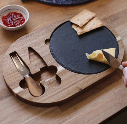 Slate & Wood Cheese Board set with knives and cheese slices on a wooden table.