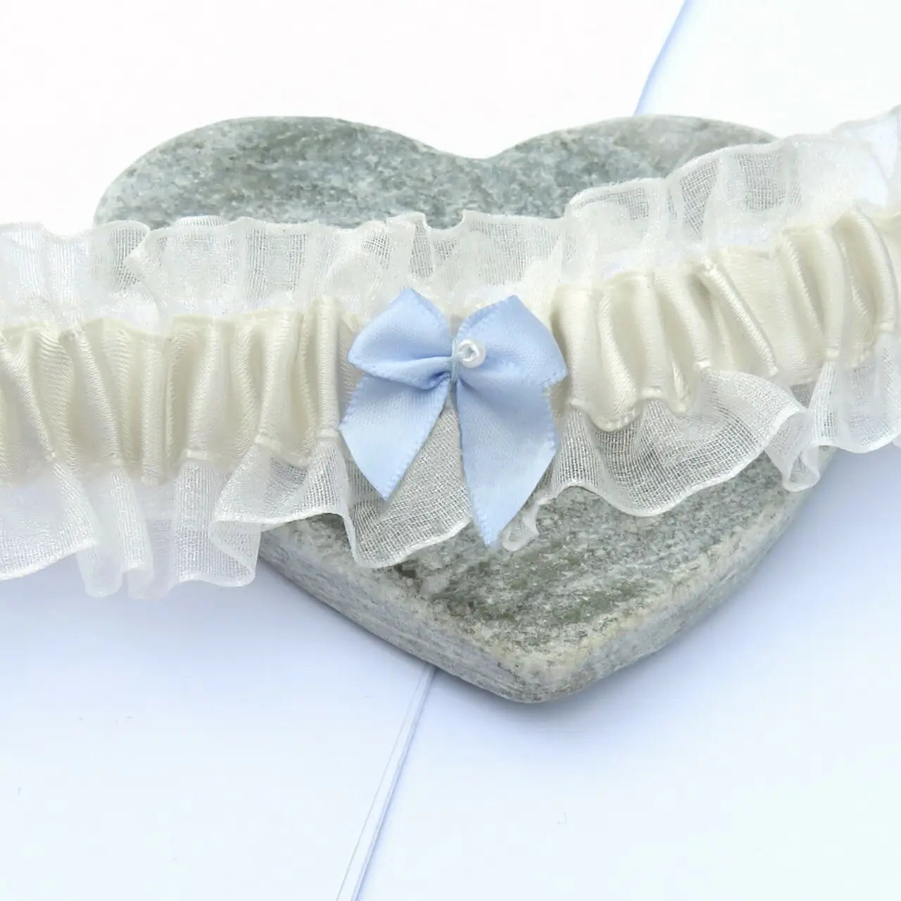 Something Blue Wedding Garter with lace and blue bow on a heart-shaped background.