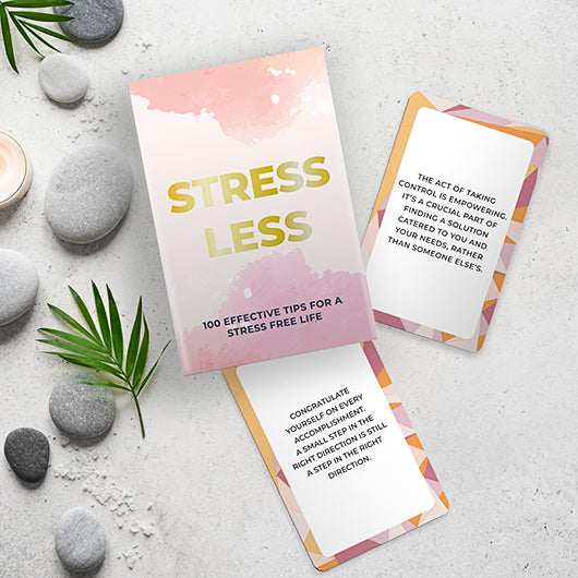 Stress Less book with cards on a gray surface with stones and leaves