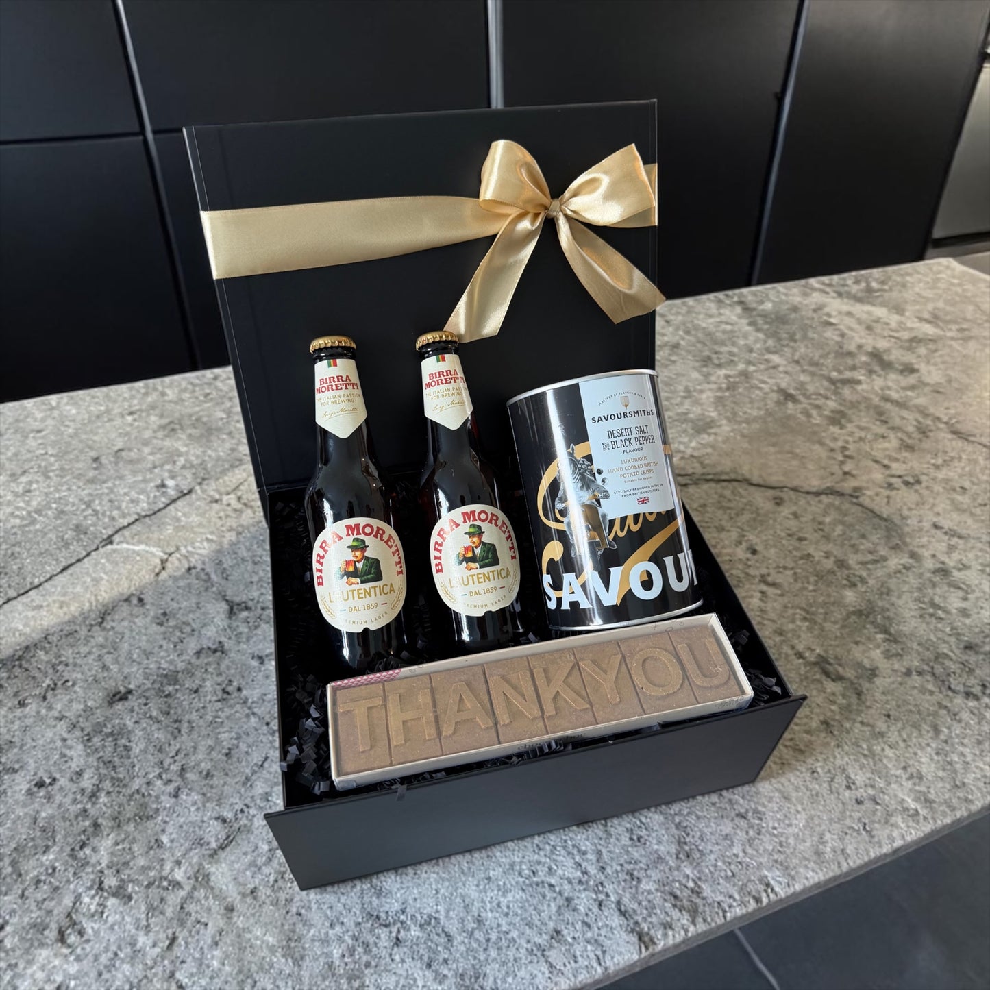 Gift set with beer bottles and a can in a black box with a gold bow on a countertop.