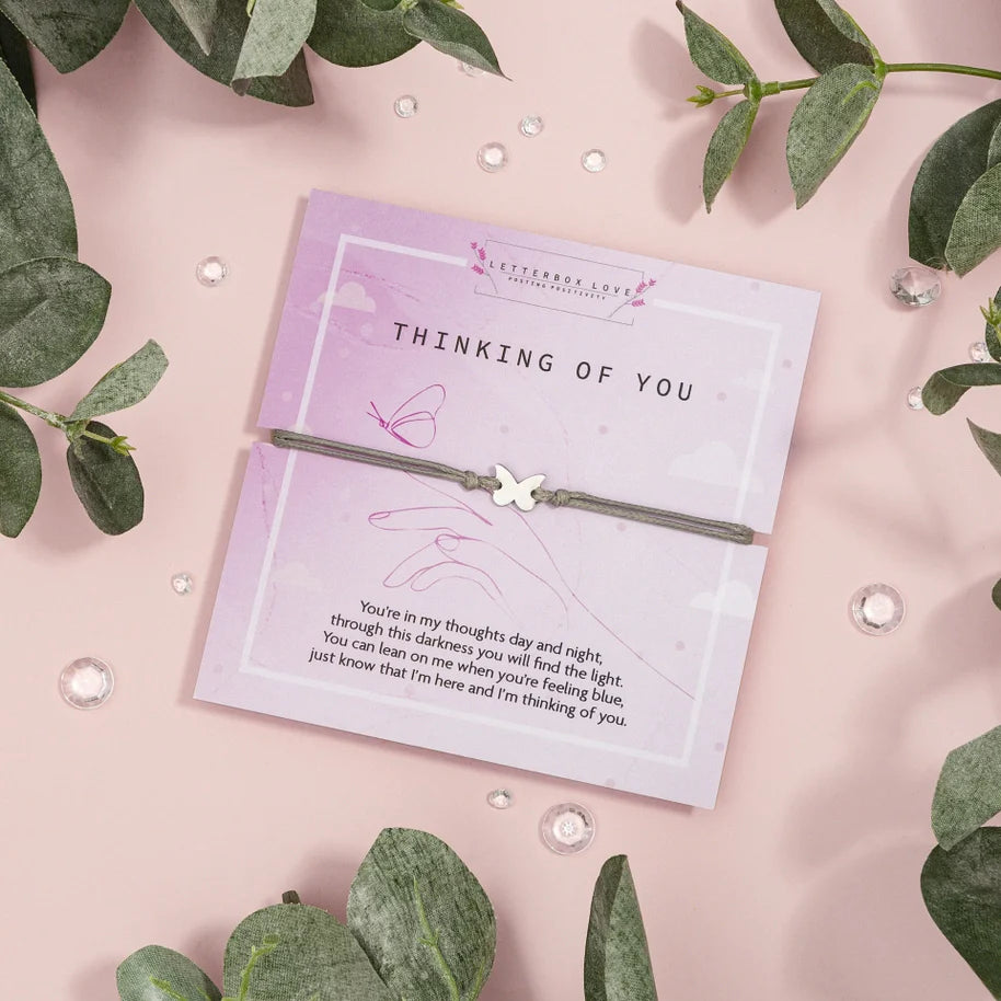 Thinking of You wish bracelet with charm and greeting card, surrounded by leaves and crystals.