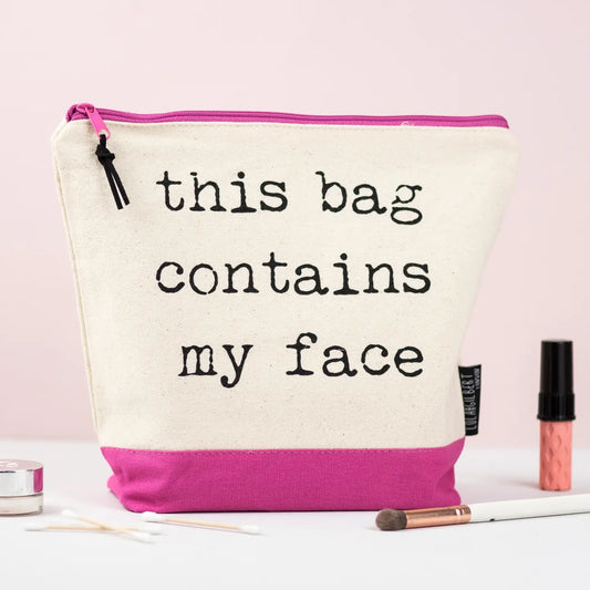Pink washbag with "This Bag Contains My Face" text, ideal for makeup lovers; durable cream canvas with water-resistant lining.