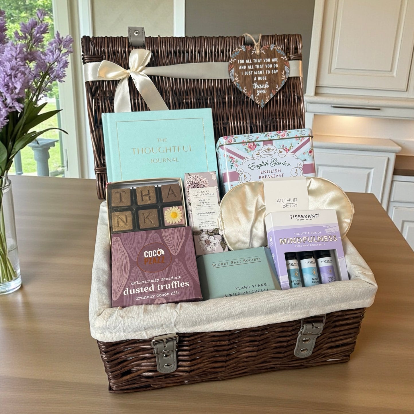 Gift basket with various items including a book and truffles on a wooden table.