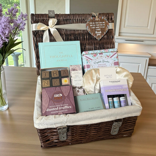 Gift basket with various items including a book and truffles on a wooden table.