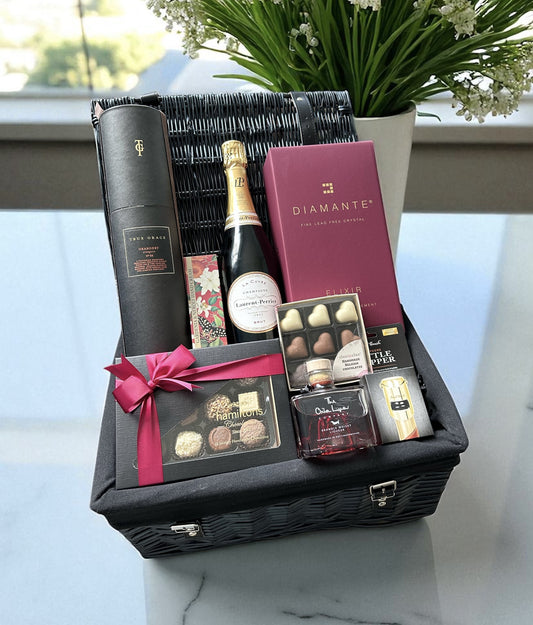Gift basket with champagne, chocolates, and other items on a marble surface.