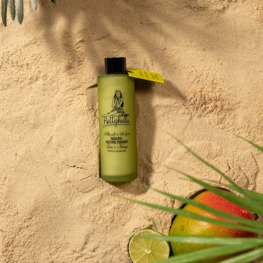 Fragrant Lime & Mango Dusting Powder on sandy background with lime and mango accents.