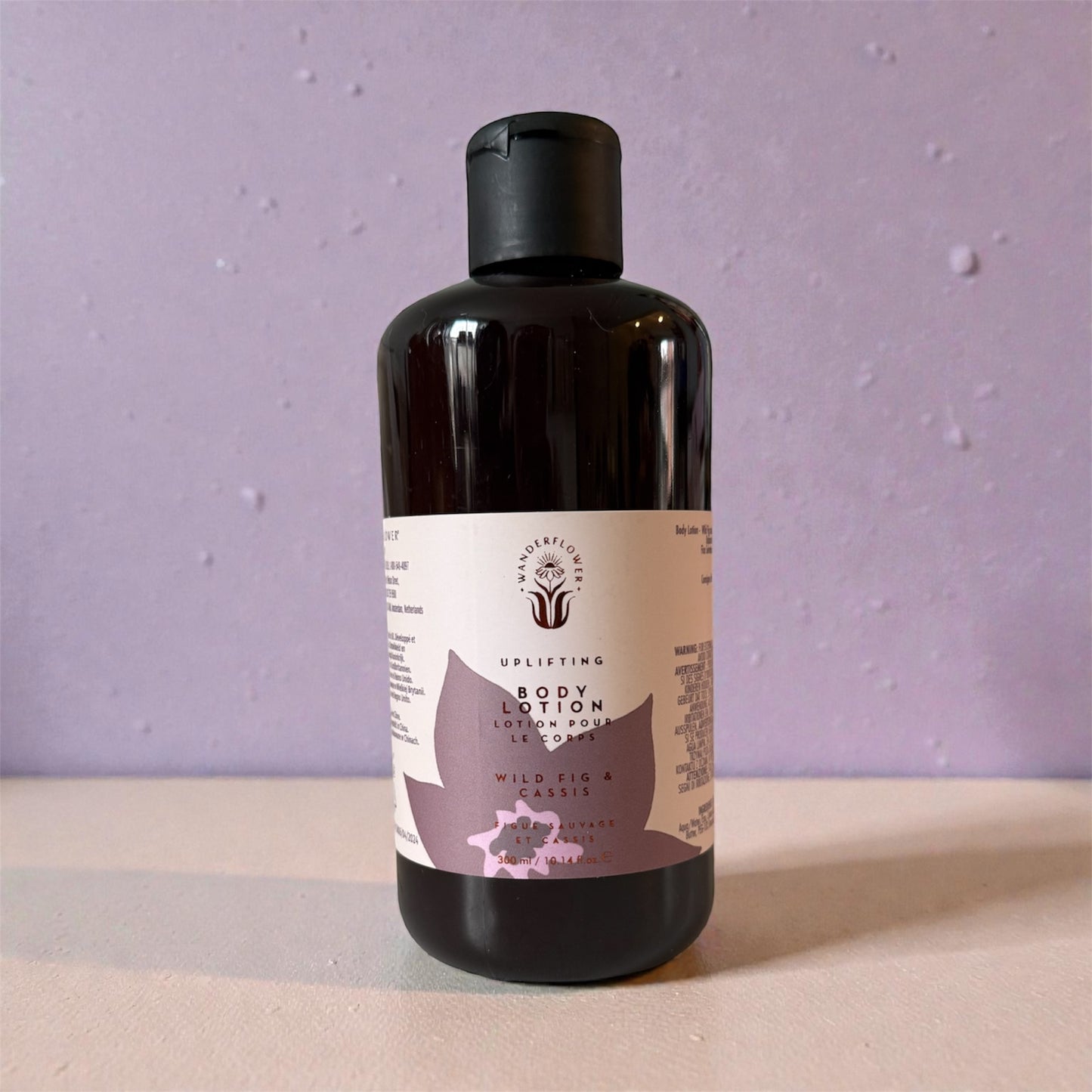 Black bottle of body wash with a label on a beige surface and purple background