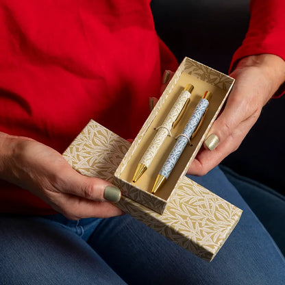 Two ornate pens in a decorative box held by a person wearing a red sweater and blue jeans.